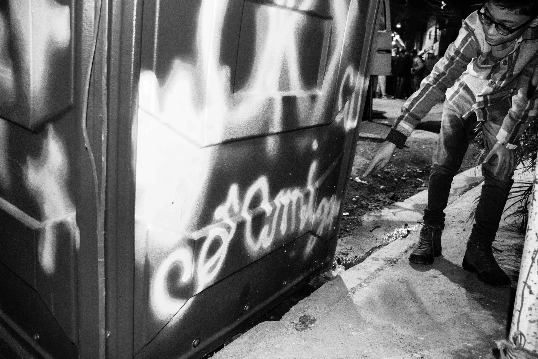 Pessoa utiliza spray para escrever em um portão, em fotografia em preto e branco