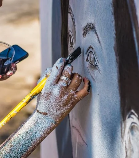 Mão com tinta trabalha os detalhes de um olho em retrato mural