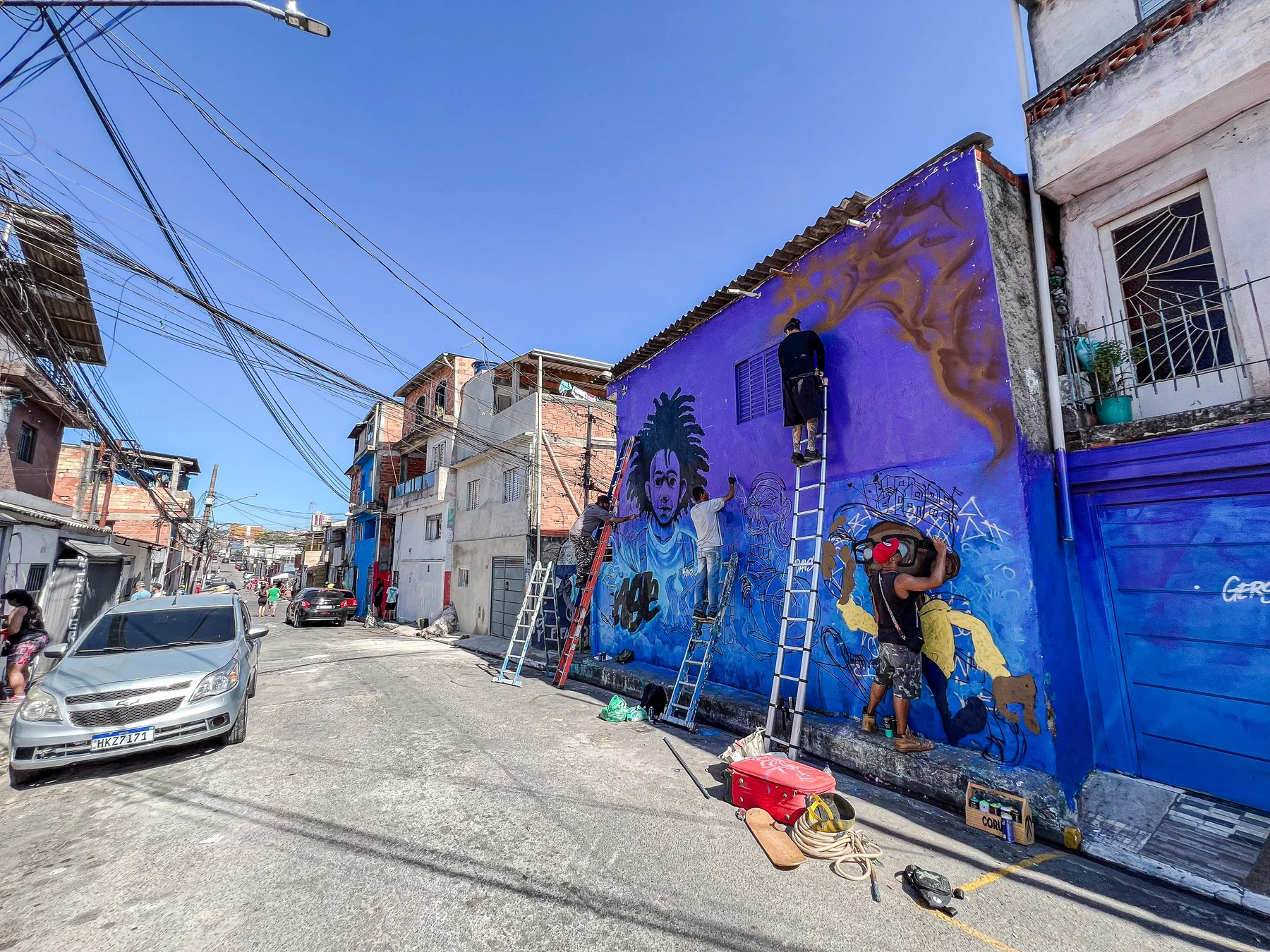 Rua com fachadas roxas e azuis, murais e artista trabalhando