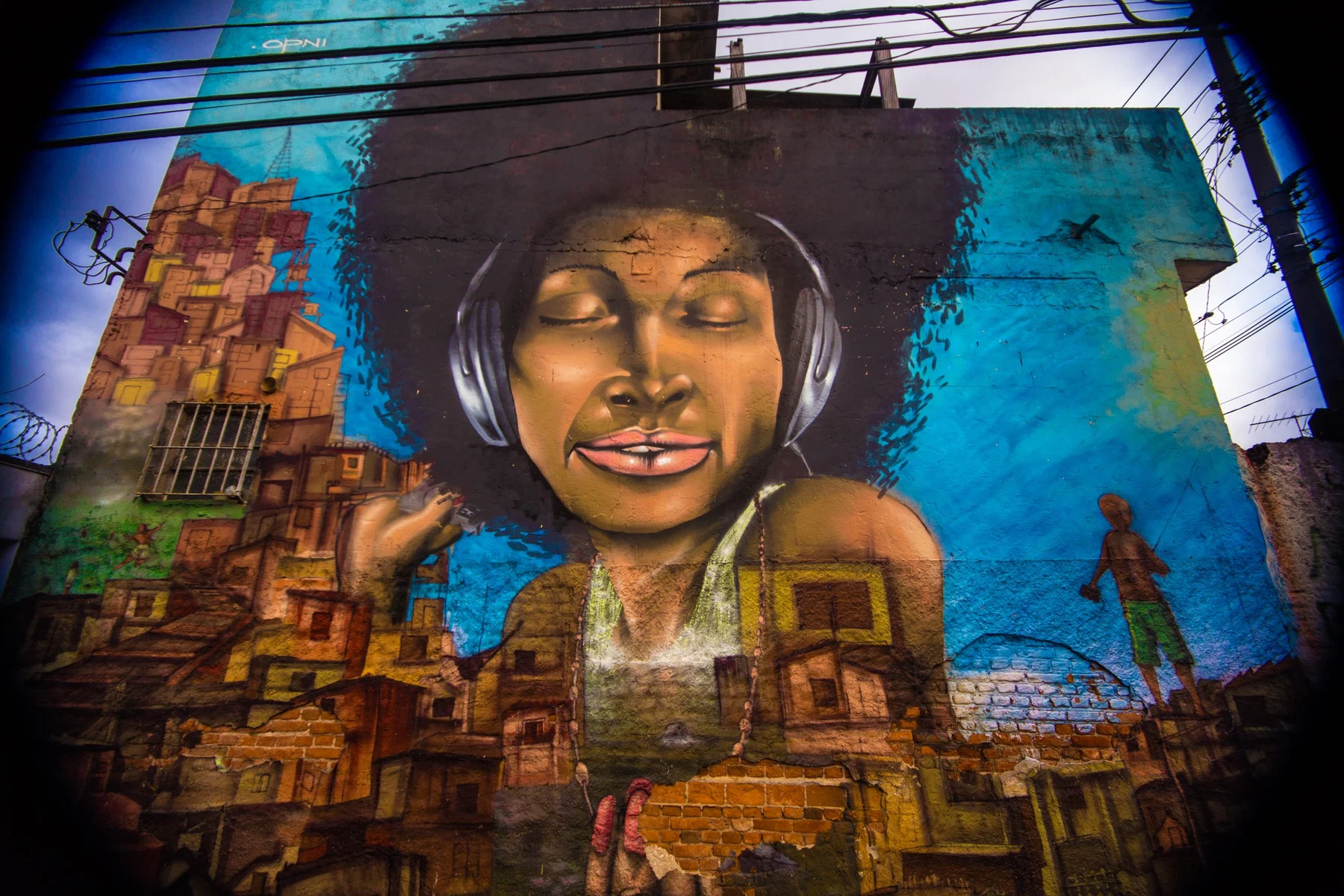 Grande retrato feminino em parede azul acima de pinturas de casas